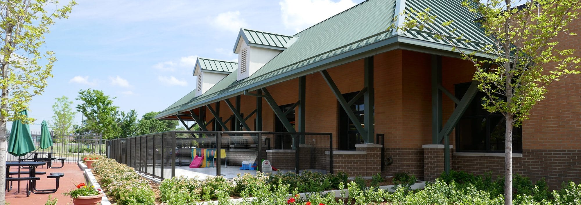 Side of the canine development center in summer. There are plants and picnic tables on red brick next to the building