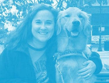 Blue colored image of a smiling woman with her arm around a golden retriever in Leader Dog harness. They are sitting outdoors