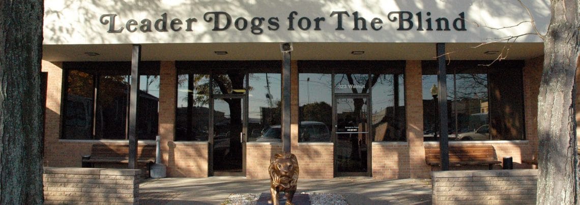 front of downtown building Front of brick building with large windows with large trees on either side. The words Leader Dogs for the Blind are across the top of the building