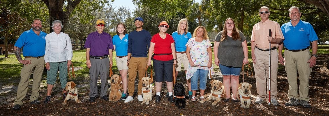 group FL clients A group of adults with guide dogs in harness and one man with a white cane stand in a line outdoors smiling at the camera