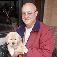 John Berkheiser holding a golden retriever puppy and smiling