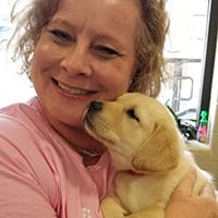 Delores Blomberg holding a yellow lab puppy and smiling at the camera