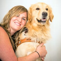 Lisa hugs golden retriever Hopper. Hopper is in leather Leader Dog harness