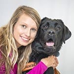 Abigail smiles at the camera while hugging black lab Yoda