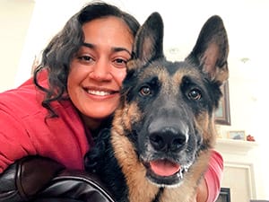 Selfie of Anu with an adult German shepherd. They are both looking into the camera and the shepherd's mouth is slightly open as if smiling with Anu.
