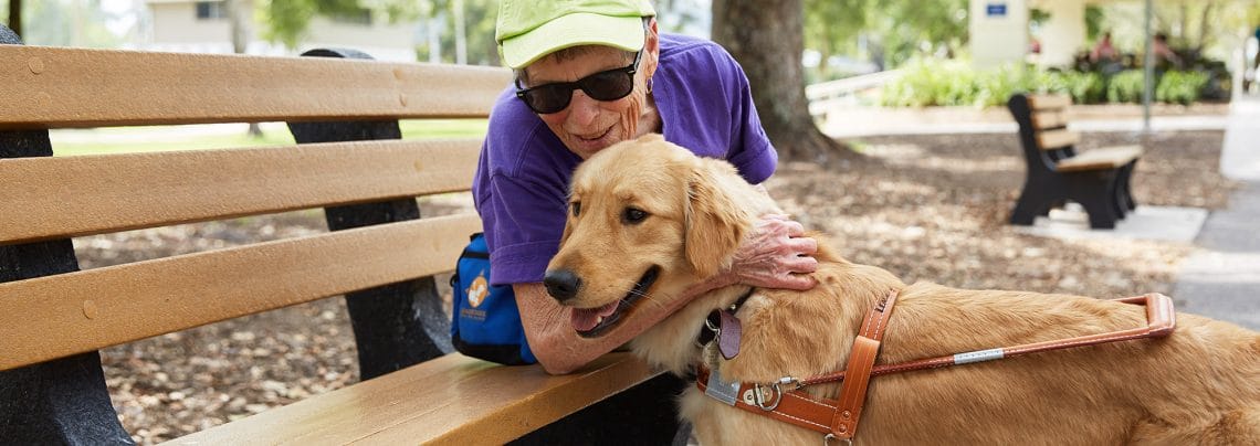 An older woman hugging a golden retriever standing in front of her. The dog is wearing a Leader Dog harness.