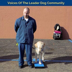 A man with a shaved haircut and goatee wearing a blue button down and the same color pants is standing next to a light-colored golden retriever which is standing with three paws on a blue training step and the fourth on the concrete next to it. At the top of the photo is text reading Voices of the Leader Dog Community.