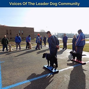 Group of men in correctional facility outfits standing outdoors with dogs on leash