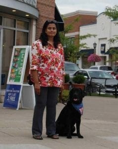Vijay stands outdoors with a black lab in a Future Leader Dog bandana