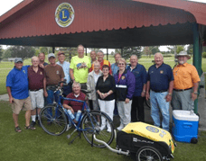 Mark stands with a group of people at an outdoor pavilion. Mark's bicycle is in front of them