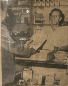 Old newspaper photo of a man behind a counter in a shop