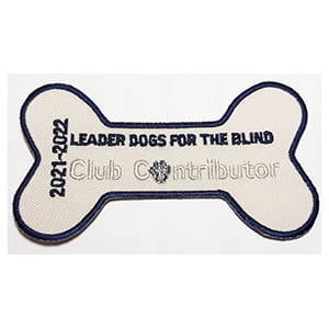 White patch in shape of dog bone with black text reading Leader Dogs for the Blind and white text underneath with Club Contributor