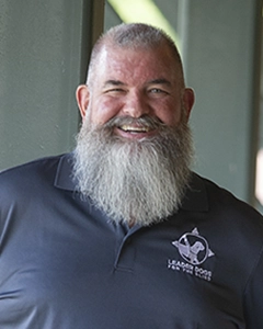 Barry, a man with buzzed gray hair and a gray beard, smiles. He's wearing a navy polo with the Leader Dog logo in white