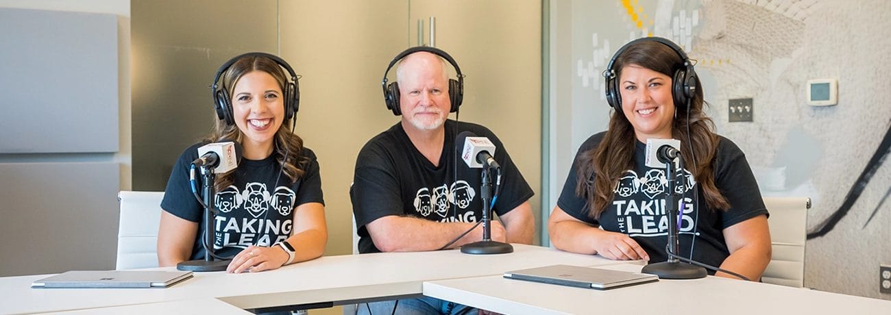 Christina, Tim and Leslie sit at a white table with microphones in front of them.