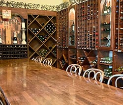 Wood table and chairs with wines in shelves along the walls behind the table