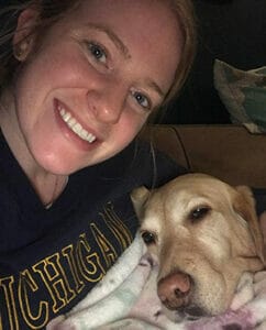 Olivia smiles in a selfie with a yellow lab lying its head on her chest