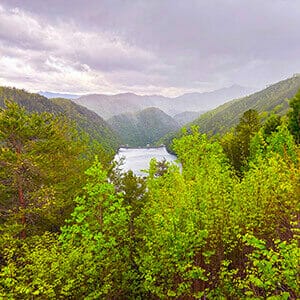 Cloudy sky over hills covered in green trees with a river running through the middle of the photo