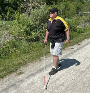 Man walking with white cane on gravel road