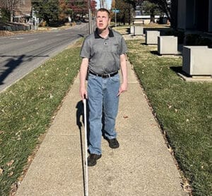 Man walking on sidewalk with white cane