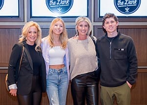 Group of three women and one man standing smiling arms around each other