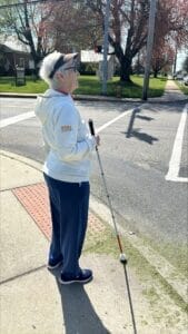 Sandy waiting to cross the street holding her white cane