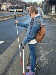 A woman standing at a curb with a white cane in one hand and a stabilizing cane in the other.