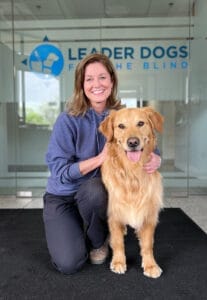 Melissa Weisse kneeling down next to a golden retriever Leader Dog.