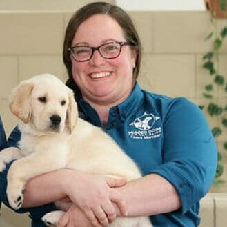 Photo of a woman in glasses smiling while holding a yellow lab puppy